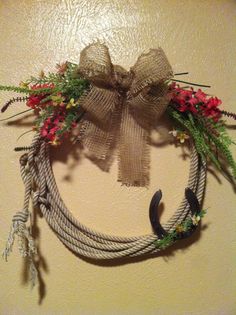 a wreath made out of rope with flowers and horseshoes hanging on the wall next to it