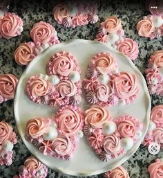 there are many pink cupcakes on the plate with white frosting and flowers