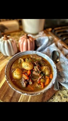 a bowl filled with stew sitting on top of a wooden table next to pumpkins