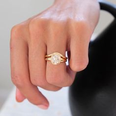 a woman's hand wearing a gold ring with a white diamond in the middle