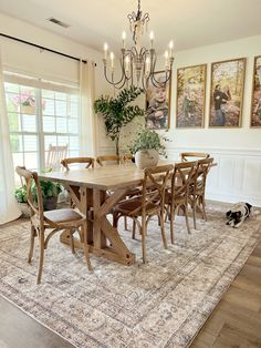 a dining room table with chairs and a rug in front of the window, next to a dog laying on the floor