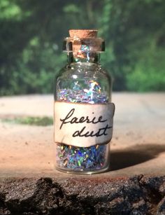 a bottle filled with lots of glitter sitting on top of a wooden table next to trees