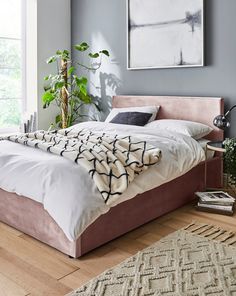 a large bed sitting next to a window on top of a hard wood floored floor