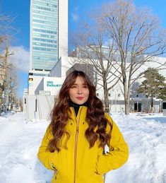 a woman standing in the snow with her hands on her hips, wearing a yellow jacket and black pants