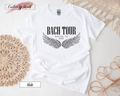 "Custom Rock and Roll Bachelorette Shirt, Bach Tour Shirt, Angel Wings Shirt, Personalized Bachelorette Shirt, Rocker Bachelorette, DG5081 H O W TO O R D E R 1️⃣Please, check and review all the photos. 2️⃣ Choose your T-shirt size and color. 🔵Different styles of shirts may have different shades of same color choice due to different manufacturer brands. 🔵For this reason, we recommend you to match shirts from the same styles if you want precisely matching colors (ex. Unisex, V-necks, Toddler, et Summer Concert Shirt With Band Logo, Summer Band Logo Shirt For Fans, Fitted Graphic Tee For Concerts, White Rock Style Top For Concerts, White Rock And Roll Top For Concert, Rock Style Fitted T-shirt For Concerts, Rocker Style Fan Merchandise Tops For Summer, Rock And Roll Bachelorette, Personalized Bachelorette