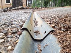 an old metal pipe laying on the ground next to a tree and some rocks in front of a house