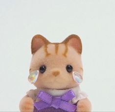 a small stuffed animal with a purple bow around it's neck and eyes, sitting on a white surface