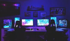 three computer monitors sitting on top of a desk in front of a purple lit wall