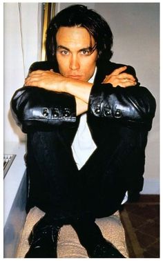 a man sitting on top of a chair wearing black leather pants and a white shirt