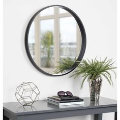 a round mirror on the wall above a table with a potted plant next to it