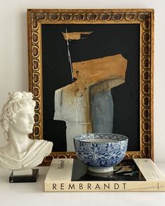 a white busturine next to a blue and white bowl on top of a book