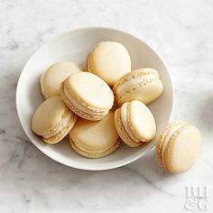 a white bowl filled with macaroons on top of a marble counter