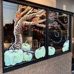 a store front window with pumpkins painted on the glass and trees in the background