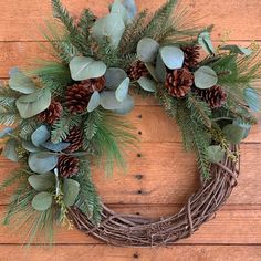 a wreath with pine cones and greenery on a wooden surface, ready to be used as a christmas decoration