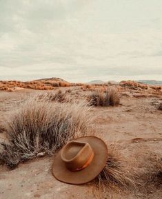 a cowboy hat sitting on top of a dry grass covered desert field with mountains in the background