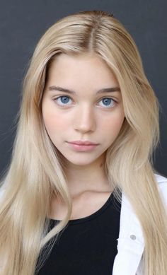 a woman with long blonde hair and blue eyes is looking at the camera while wearing a white jacket