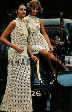 two women in dresses sitting on the hood of an old car, posing for a photo