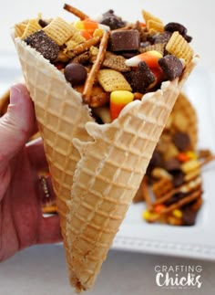 a person holding an ice cream cone filled with candy corn, chocolate chips and cheetos