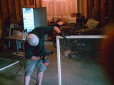 a man in black shirt and white helmet working on a table with a driller