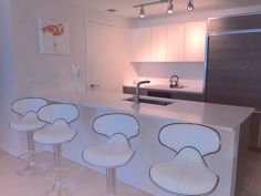 three white bar stools sitting in front of a kitchen counter with an oven and sink