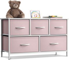 a teddy bear sitting on top of a chest of drawers with pink drawers and white handles