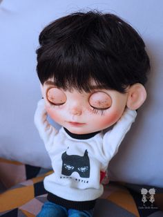 a close up of a doll laying on a bed with its eyes closed and hands behind his head