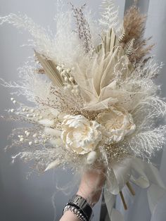 a woman's hand holding a white bouquet with feathers and flowers on top of it