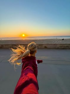 a woman standing on top of a beach next to the ocean with her hair flying in the air