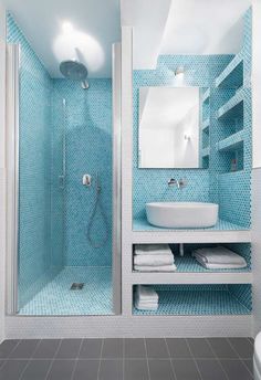 a bathroom with blue tiles and a white sink under a mirror next to a walk in shower