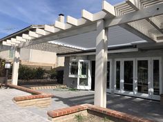 an outdoor patio area with white pergolia and brick steps leading up to the front door