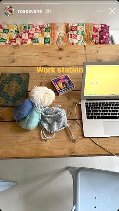 a laptop computer sitting on top of a wooden table next to a pile of yarn