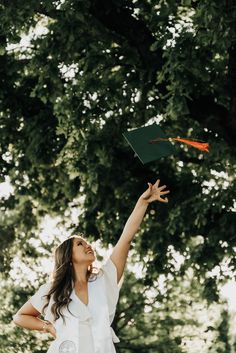 a woman in white shirt flying a green and orange kite with trees in the background