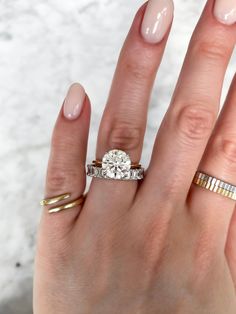 a woman's hand with two rings and a ring on her finger, holding an engagement ring