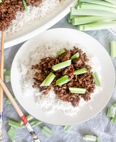 two plates filled with rice and meat next to chopsticks on a tablecloth