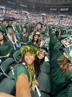 graduates in green caps and gowns smile at the camera while sitting in chairs with leis on their heads