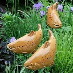 three brown fish statues sitting on top of green grass and purple flowers in the background