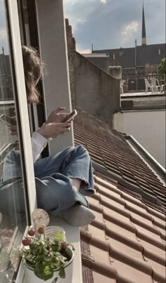 a woman sitting on top of a window sill looking at her cell phone