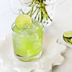 a green drink with lime slices on the rim and in a bowl next to it