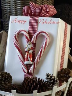 a gift wrapped in red and white ribbon sitting on top of a basket filled with pine cones