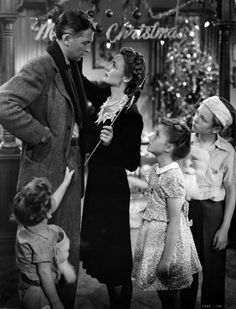 an old black and white photo of people standing in front of a christmas tree