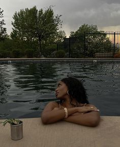 a woman sitting on the edge of a swimming pool with her arms crossed and looking off into the distance