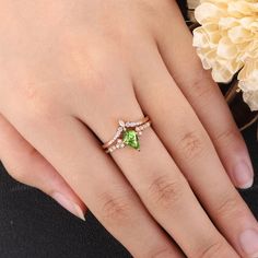 a woman's hand holding a ring with two stones on it and a flower in the background