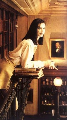 a woman sitting on top of a wooden table next to a book shelf filled with books