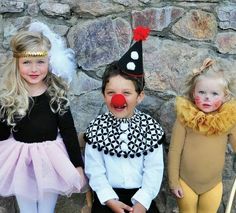 three children dressed up in clown costumes standing next to a stone wall and posing for the camera