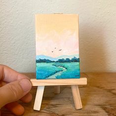 someone is holding up a miniature easel with a painting on it's side