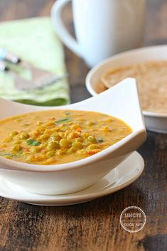 there is a bowl of soup on the table next to two plates with spoons