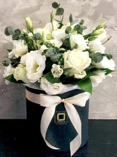 a bouquet of white flowers in a black box with a ribbon around the bow on a table