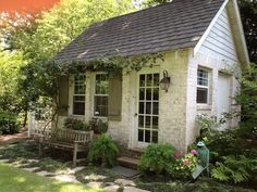 a small white house sitting in the middle of a lush green yard with lots of trees