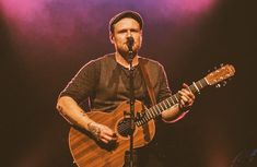 a man holding a guitar while standing in front of a microphone on top of a stage