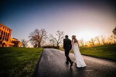 a bride and groom walking down the road at sunset in front of an old building